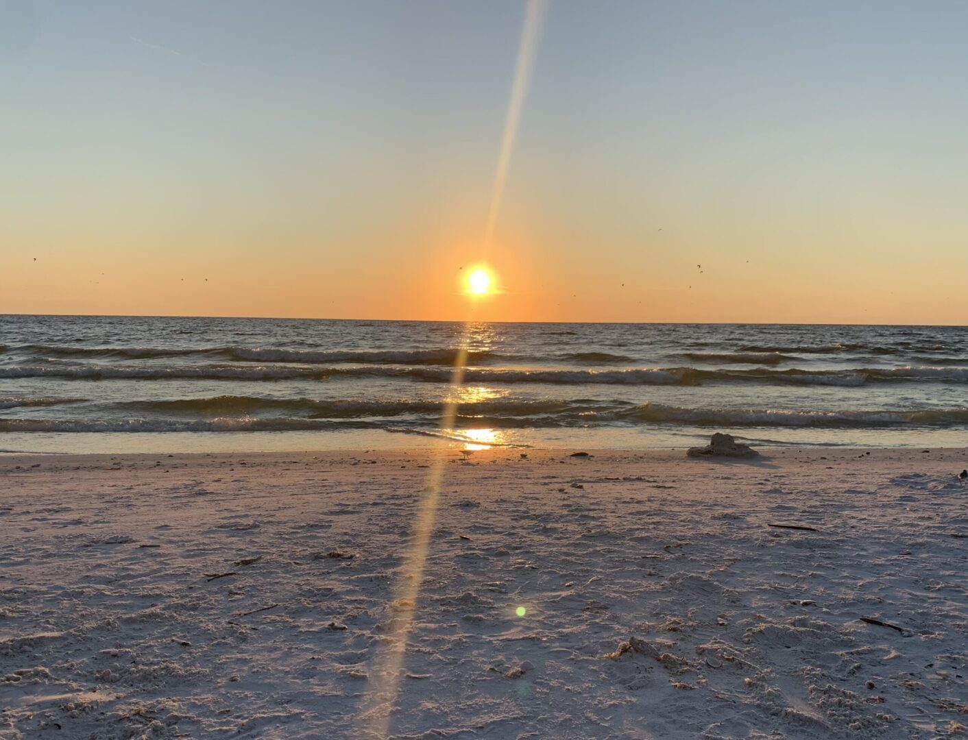 A sun setting over the ocean on a beach.